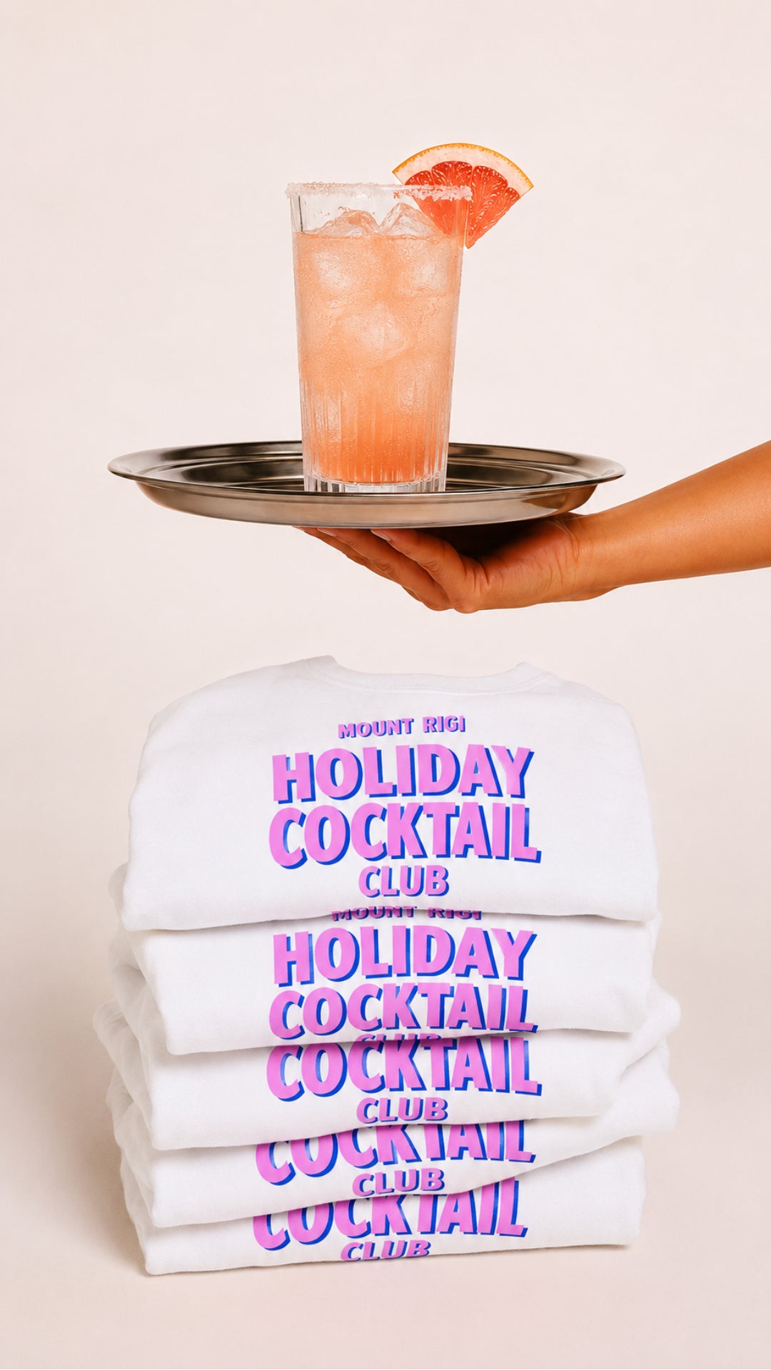 Mount Rigi Holiday Cocktail Club grapefruit cocktail served on a tray above stacked Holiday Cocktail Club T-shirts.